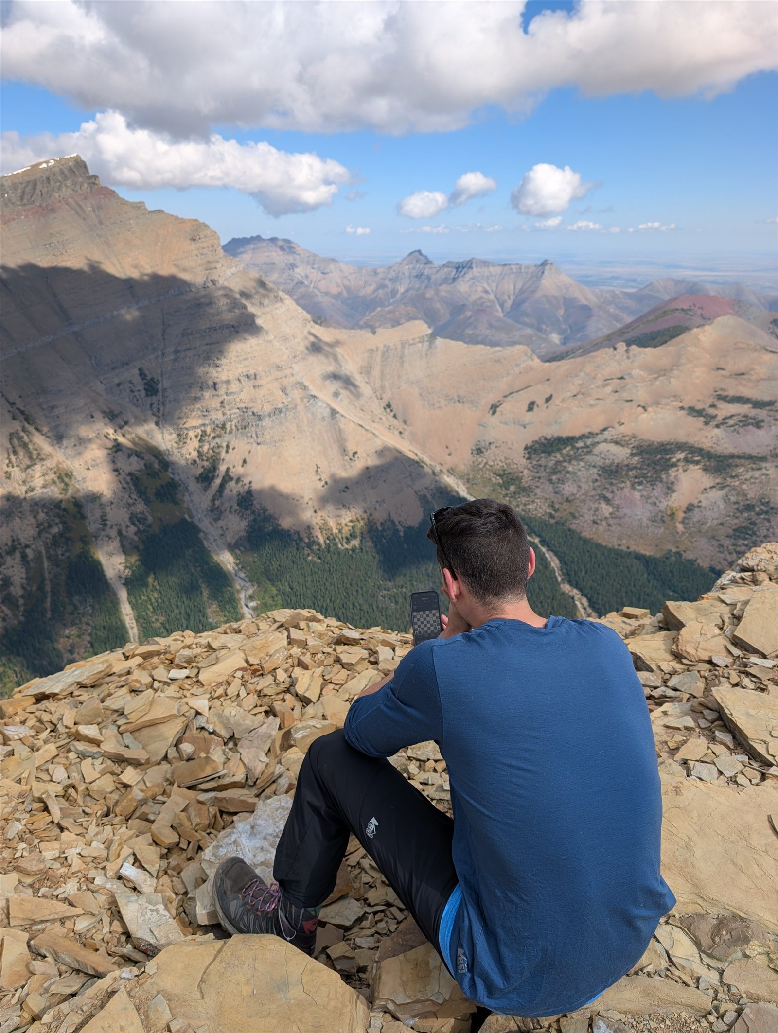 A hiker seated on rocky ground overlooking lakes and mountain cliffs