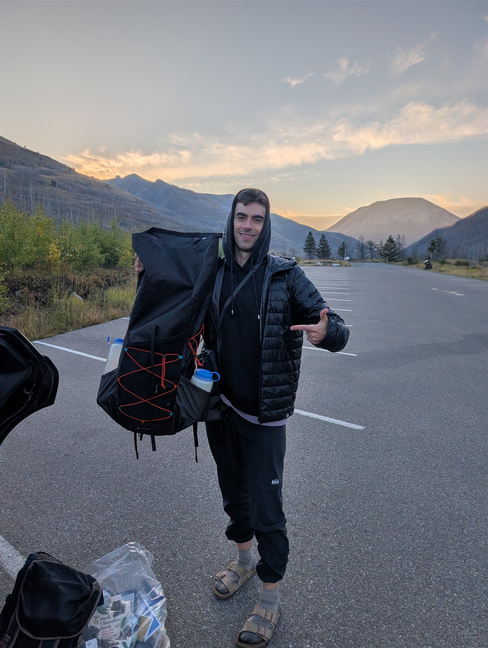 A backpacker holding a loaded pack beside the car in the early light