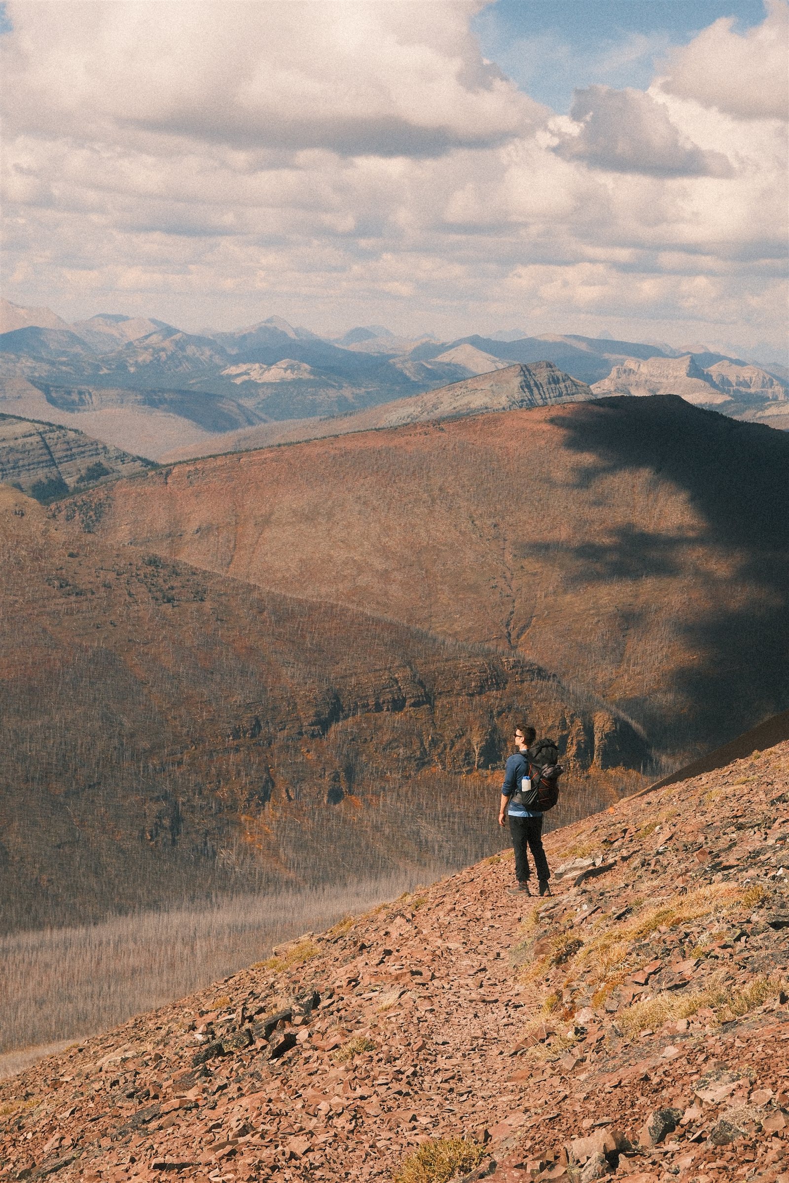 A lone backpacker on a rocky slope above a broad valley and distant mountains