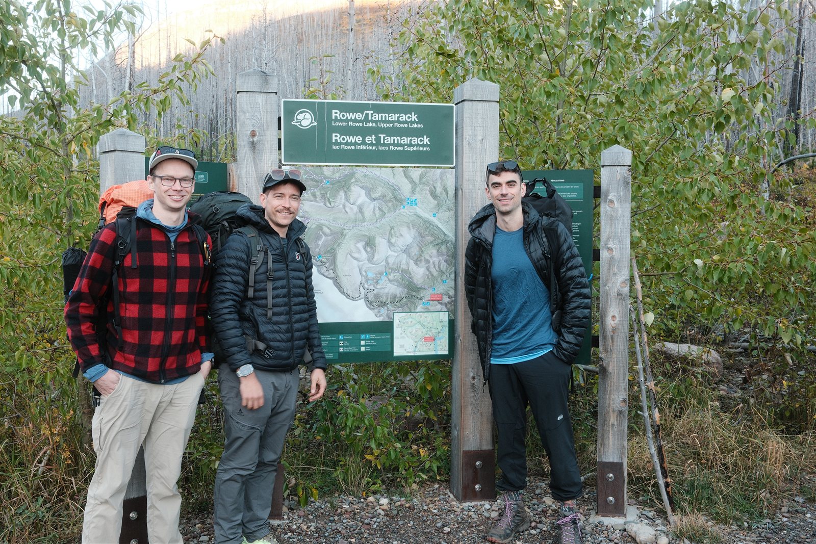Three backpackers standing beside the Rowe/Tamarack trailhead sign
