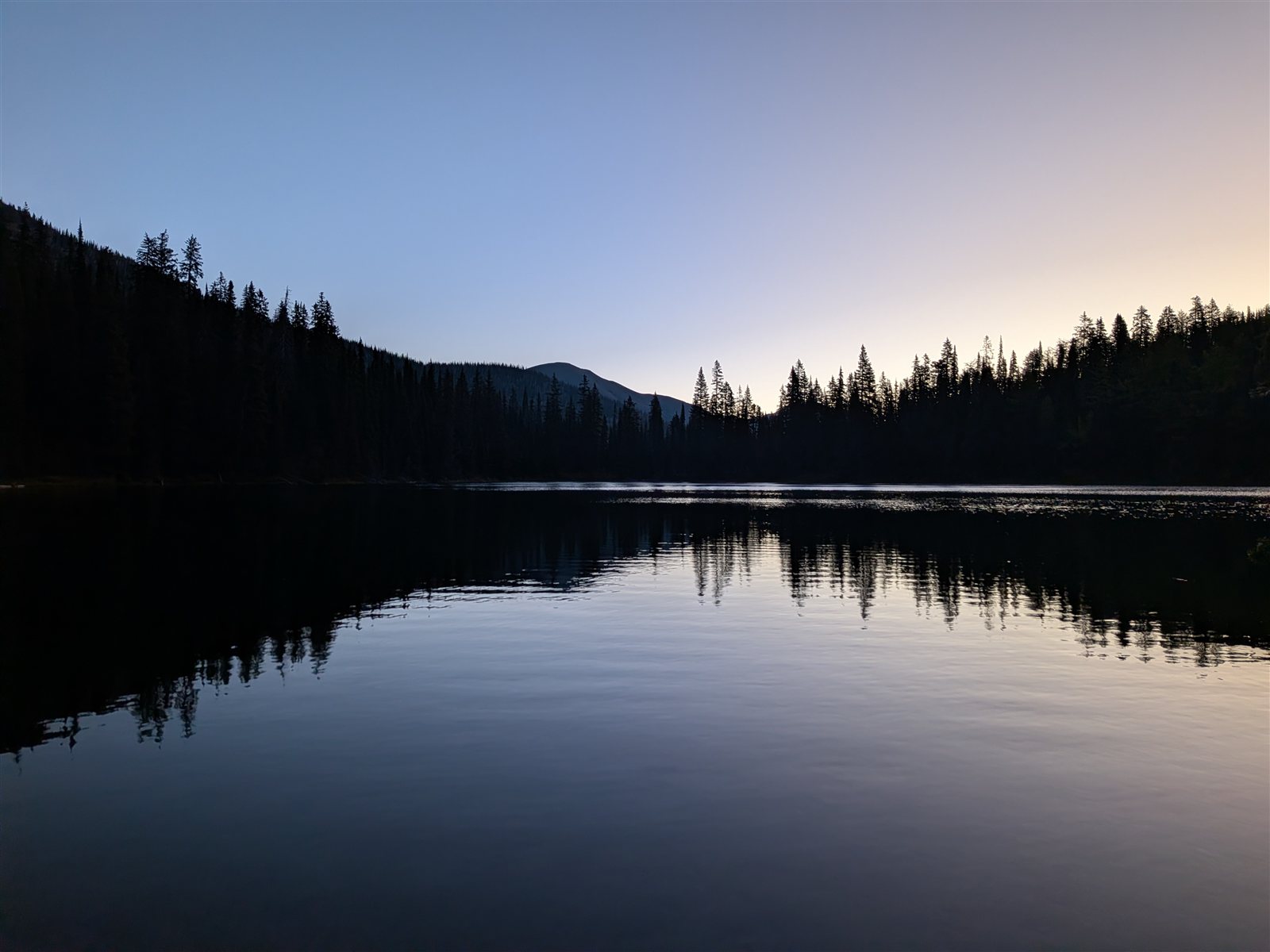 Still water at Upper Twin Lake reflecting dark trees beneath a pale morning sky