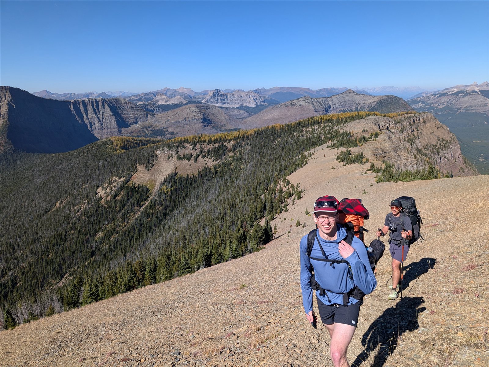 Two backpackers climbing a rocky trail on Avion Ridge with mountains behind them